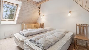 Une chambre avec deux lits, un berceau en bois, une chaise en bois et une lucarne.
