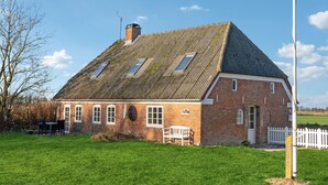 Une maison en briques avec un toit à pignon très incliné, de nombreuses fenêtres et un petit porche avec un banc.