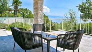 A terrace with wicker chairs and a table, overlooking a scenic view of the sea and greenery. - Awesome home in Opatija (Opatija)