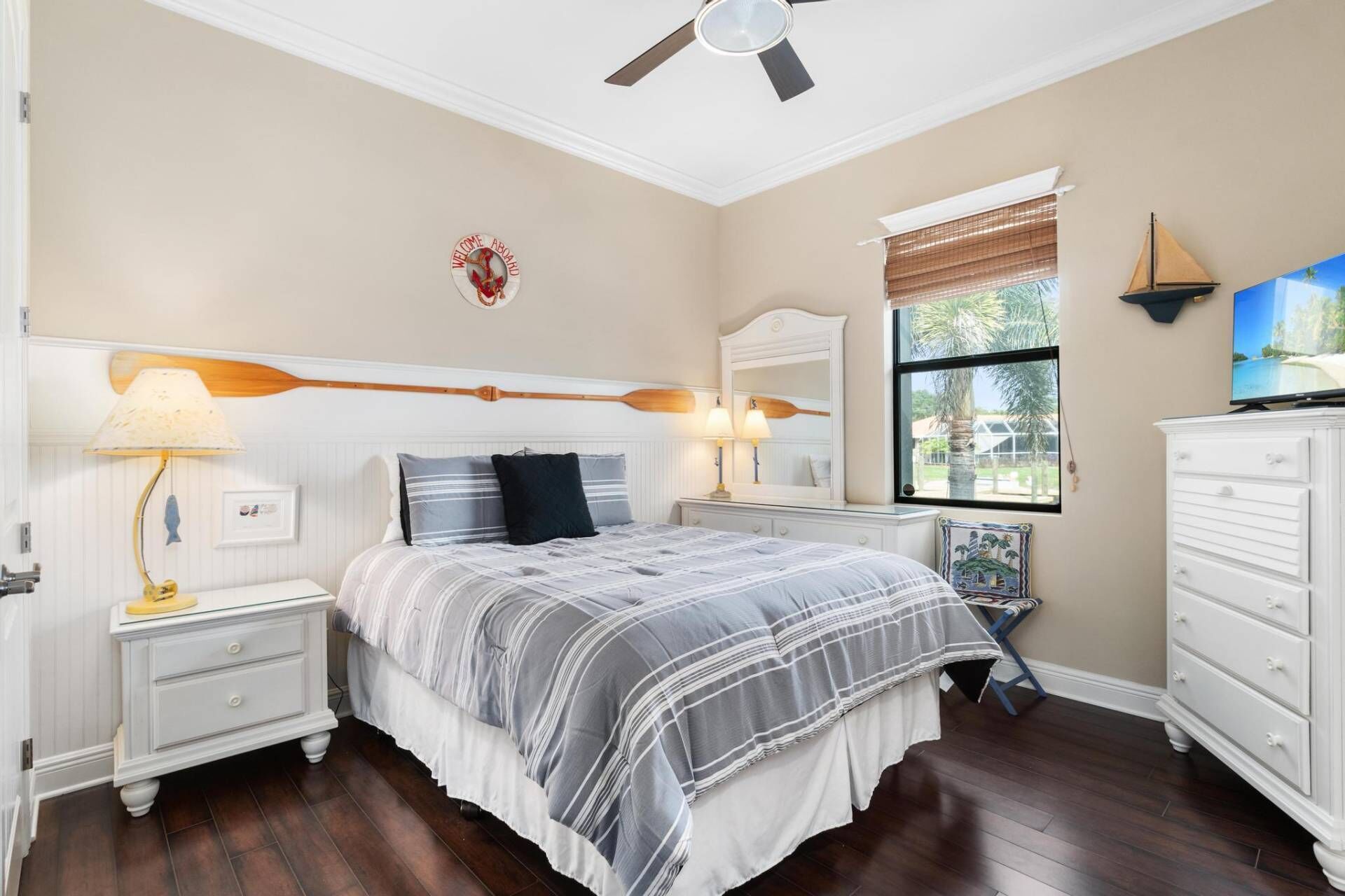 A bedroom with a bed, nightstands, a dresser, a ceiling fan, a window with blinds, and a television.