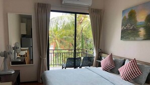 A bedroom with a bed, a desk, a chair, and a balcony with a view of greenery. - Title by Villacarte (Tambon Rawai)