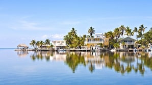Une propriété située au bord de l’eau, dotée d’une piscine, d’une structure à toit de chaume et de plusieurs bâtiments avec des balcons donnant sur l’eau.