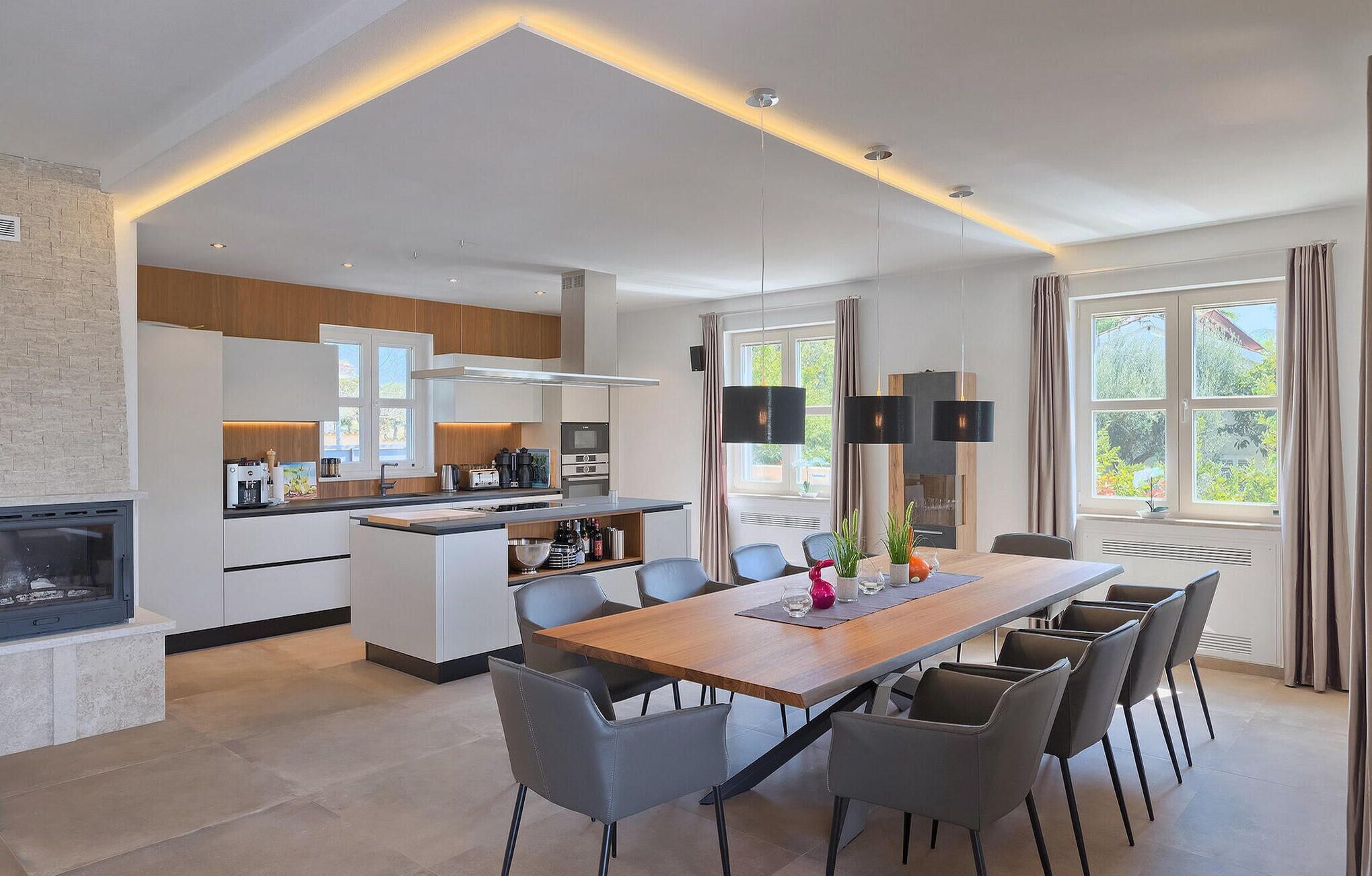 Une cuisine moderne dotée d’un îlot central, d’appareils électroménagers intégrés et d’un coin repas avec une longue table et des chaises.