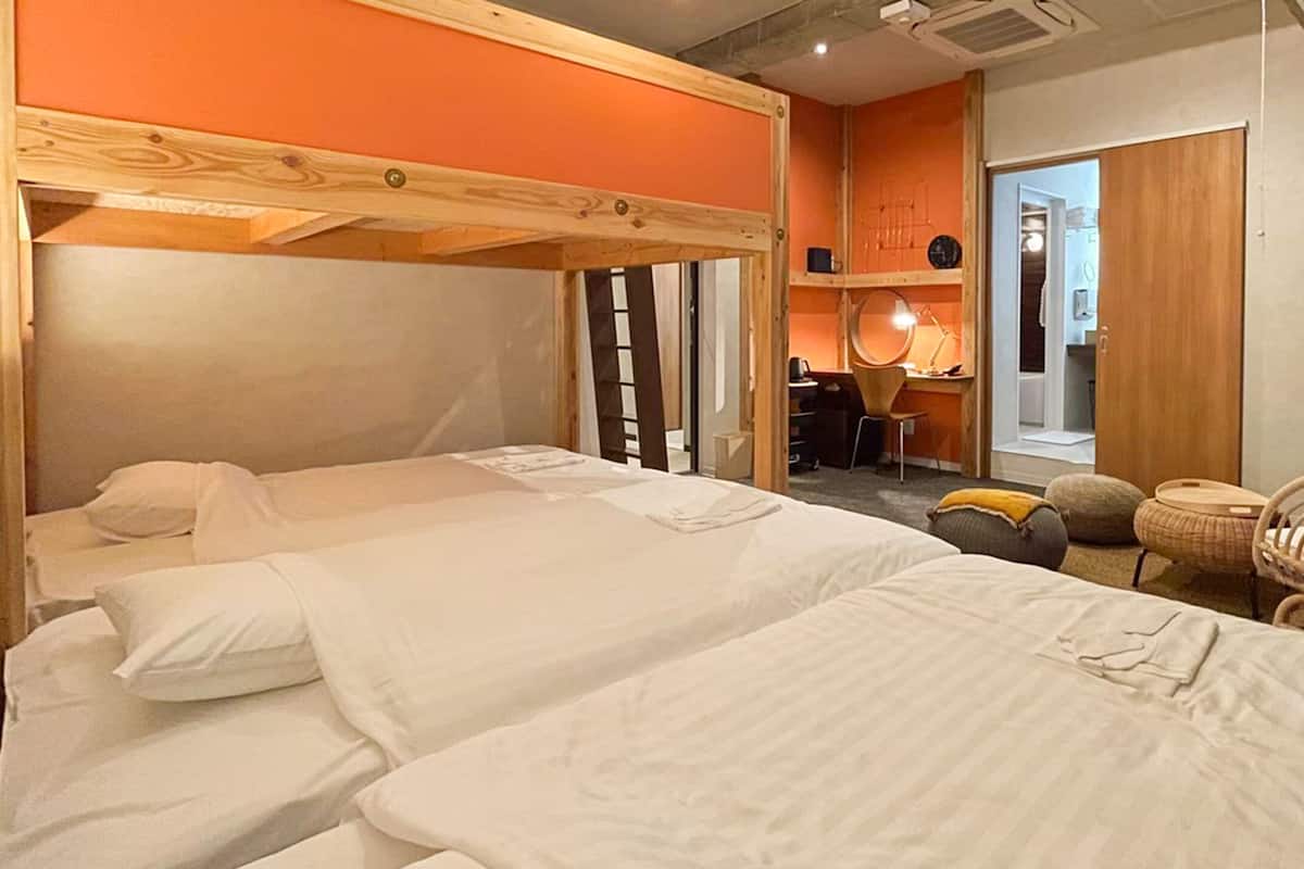 A hotel room with two beds, a wooden headboard, a desk with a chair, a small table, and a basket.