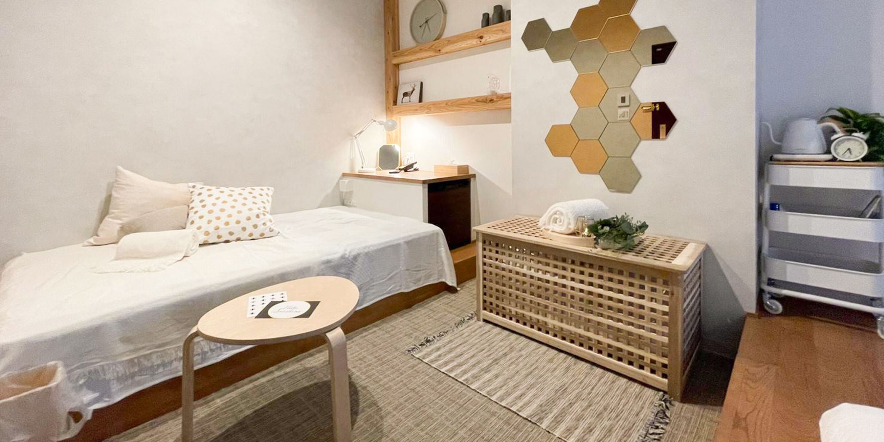 A neatly arranged bedroom with a bed, bedside table, lamp, and a wall-mounted clock.