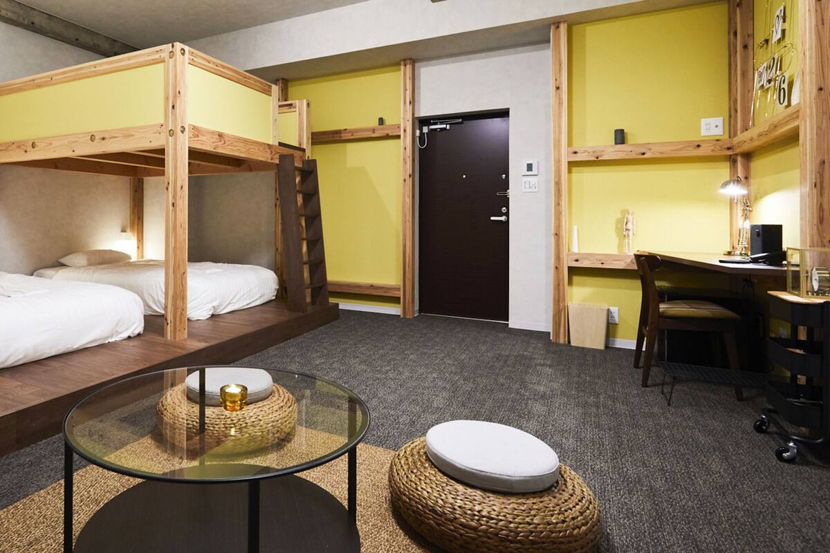 A room with bunk beds, a small round table, a chair, a desk, and a computer.