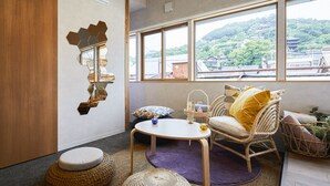 A modern room with a large window, a wooden door, a round seating area, and a wall-mounted mirror. - Mange Tak Resort Onomichi (Onomichi)