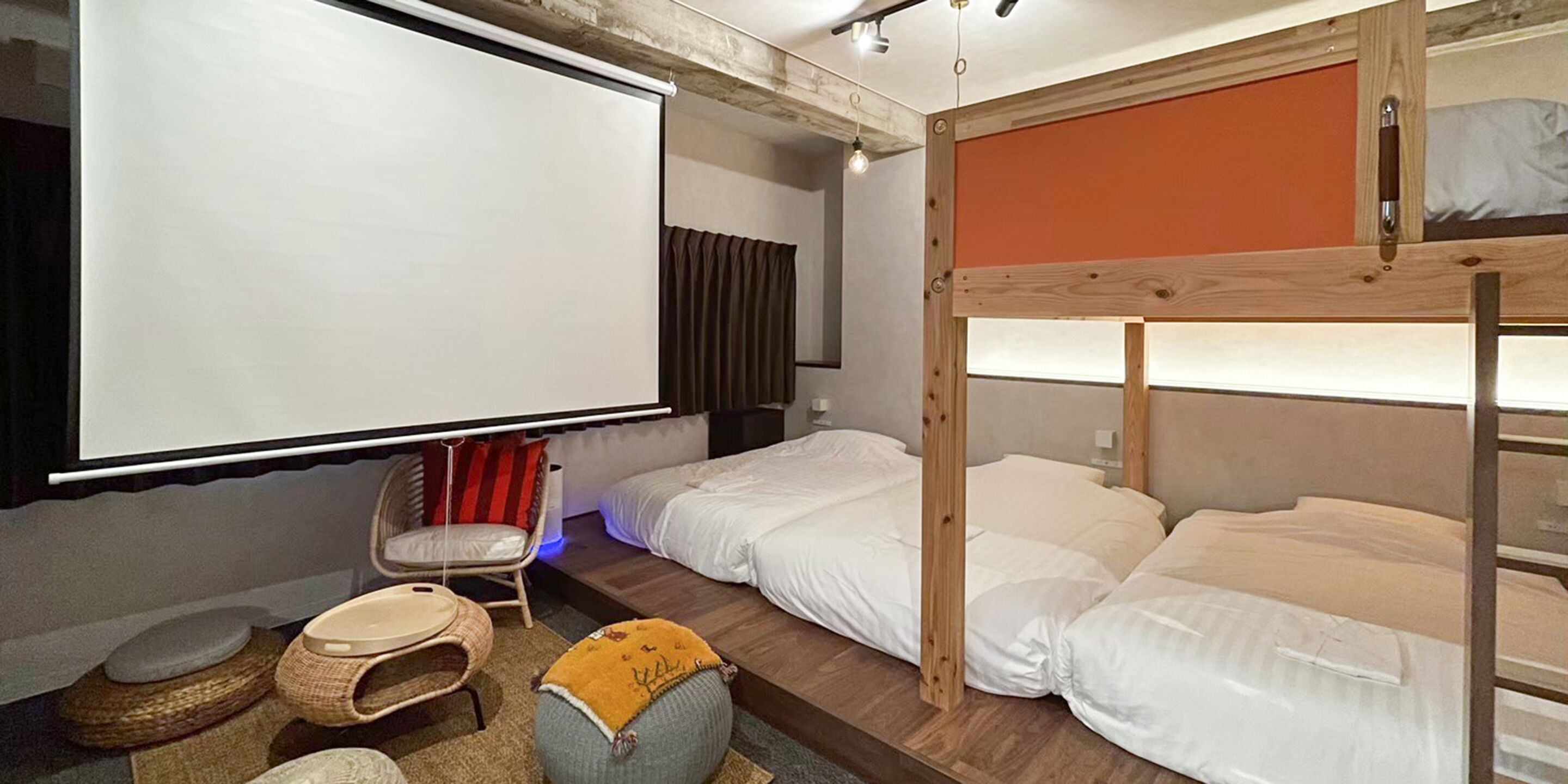 A room with bunk beds, a projector screen, a chair, and a small table.