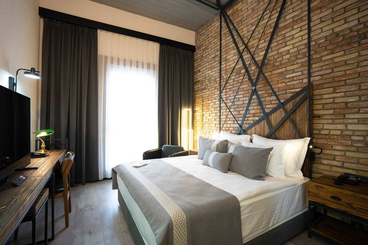 A hotel room with a large bed, a desk with a lamp, and a brick wall.