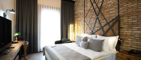 Habitación de hotel con una cama grande, un escritorio con lámpara y una pared de ladrillo.