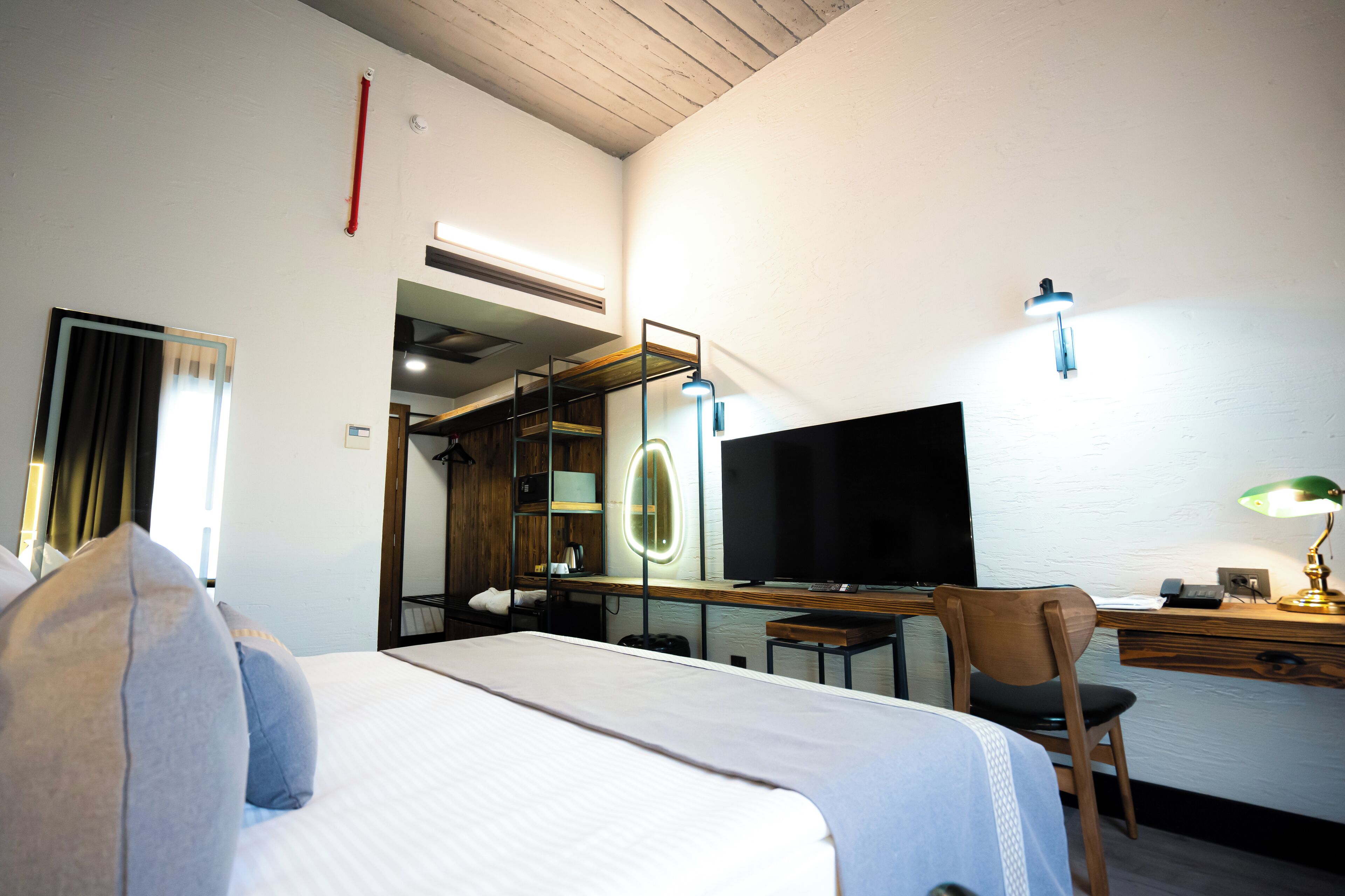 Ein Hotelzimmer mit Bett, Schreibtisch, Stuhl, Fernseher und Spiegel.