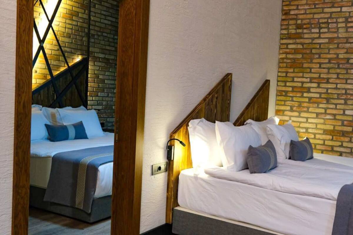 A hotel room with a brick wall, a wooden headboard, and a bed with white bedding and multiple pillows.