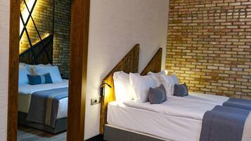 A hotel room with a brick wall, a wooden headboard, and a bed with white bedding and multiple pillows.