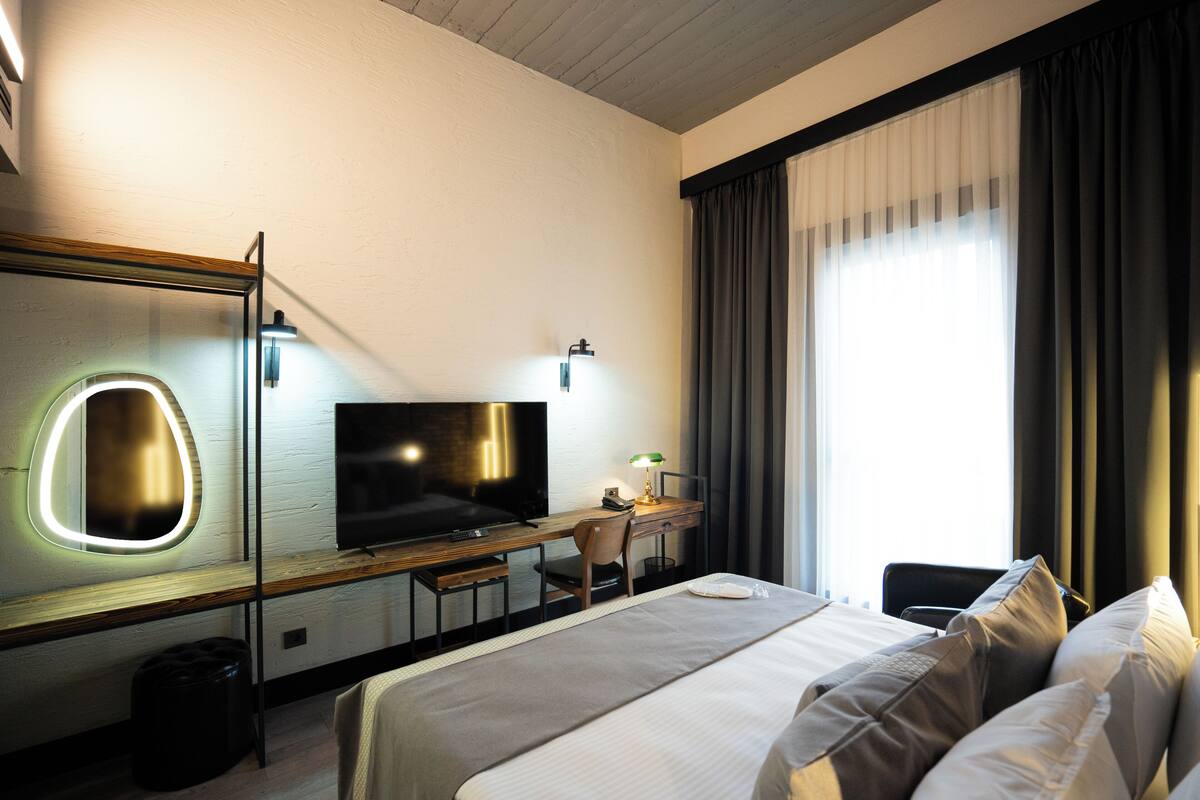 A hotel room with a bed, a desk with a chair, a television, and a large mirror.