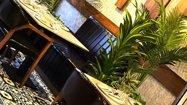 A dining area with a long table set for a meal, surrounded by chairs, with potted plants and a wooden wall with recessed lighting. - Rest & More by Dedeman Mersin Erdemli (Erdemli)