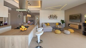 Eine moderne Küche mit Kochinsel, ein Essbereich mit großem Tisch und ein Wohnzimmer mit Sofa und Zierkissen.