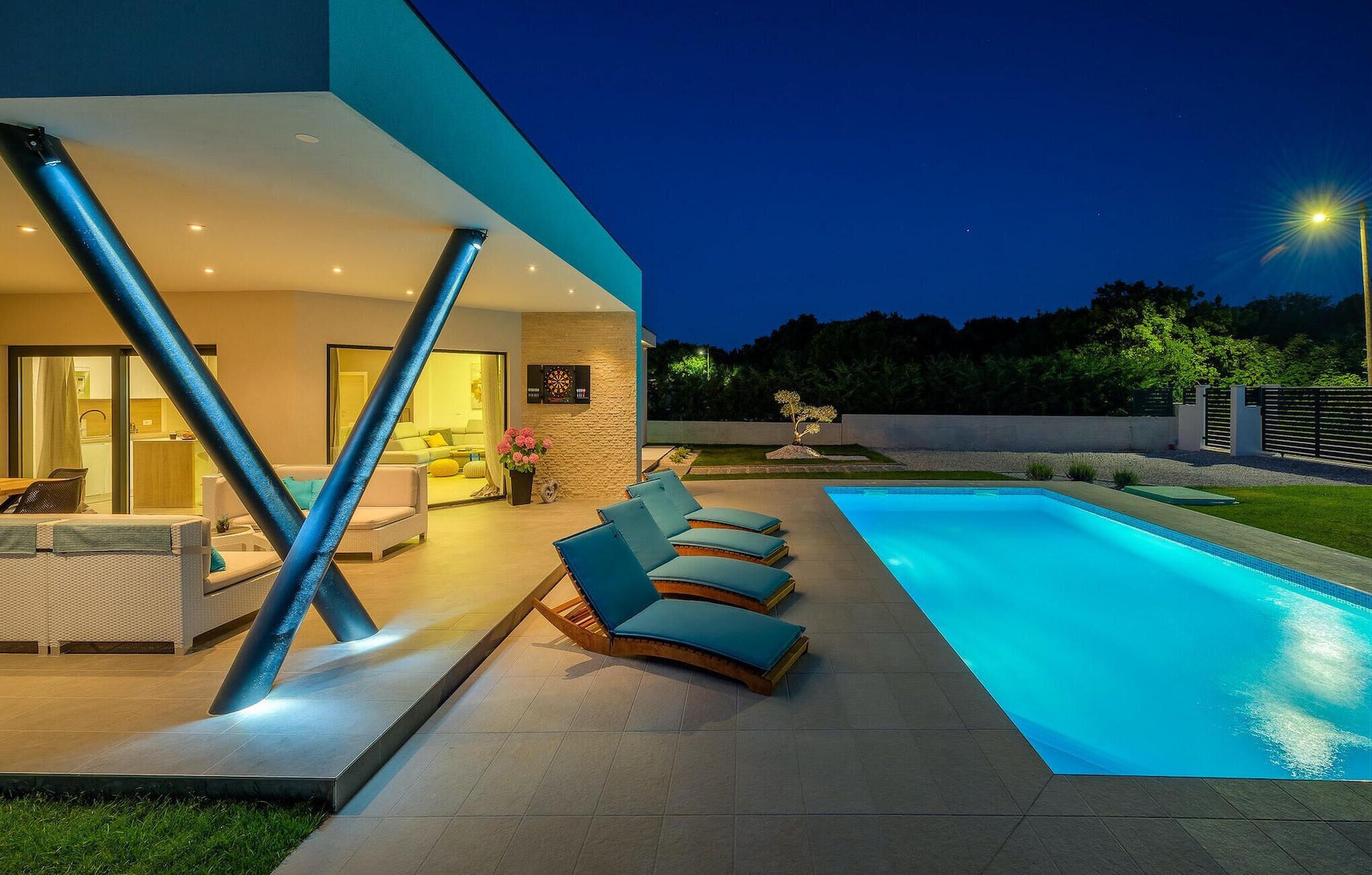 A modern outdoor pool area with lounge chairs, a well-lit patio, and a view of the surrounding landscape.