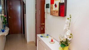 Ein Flur mit einer Holztür, einer weißen Wand mit einer Dekoration, einer weißen Theke mit einer Blumenvase und einem kleinen Tisch mit einer Kerze.
