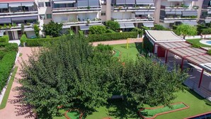 Eine angelegte Grünfläche mit einem großen Baum, einem Spielplatz und einem Gebäude mit mehreren Balkonen.