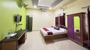 A bedroom with a bed, a desk, a television, an air conditioning unit, and a wardrobe. - Green Reed Homestay (Bokakhat)