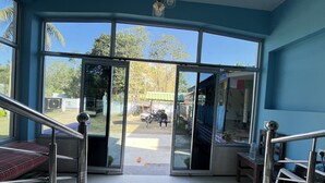 A room with a large glass door leading outside, a metal staircase, and a view of the outside area including a parked motorcycle and a green structure. - Green Reed Homestay (Bokakhat)