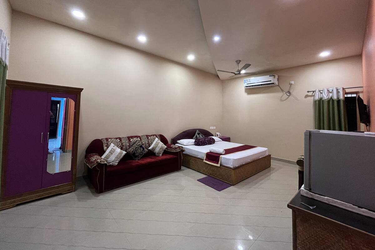 Quarto com cama, sofá, televisão e ar condicionado.