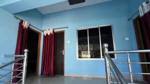 A room with a blue wall, a window, a door, and a staircase with metal railings. - Green Reed Homestay (Bokakhat)
