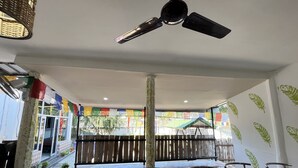 A dining area with a ceiling fan, a table with chairs, colorful flags, and a view of the outside. - Green Reed Homestay (Bokakhat)