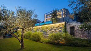 A modern two-story house with a stone facade, a visible balcony, and a well-maintained lawn.