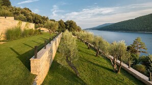 A landscaped area with a stone wall, a grassy lawn, and trees.