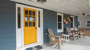 A house with a yellow front door, a porch with Adirondack chairs, and a welcome mat with an anchor symbol. - Pet-Friendly Tilghman Island Coastal Retreat (Tilghman Island)