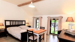 A bedroom with a bed, bedside tables, a wooden dining table, chairs, and a view of the outdoors through a window. - Arnoltice 9 by Interhome (Arnoltice)