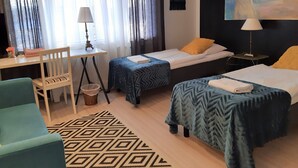 Una habitación de hotel con dos camas individuales, un escritorio con lámpara, una silla y un cuadro en la pared.