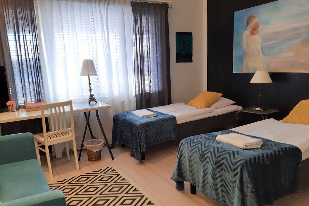 Une chambre d’hôtel avec deux lits simples, un bureau avec une lampe, une chaise et un tableau au mur.