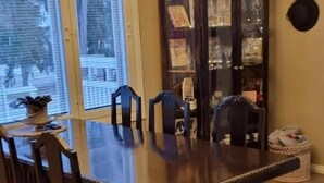 Comedor con una amplia mesa de madera, seis sillas, una araña, un reloj y un aparador con cristalería.