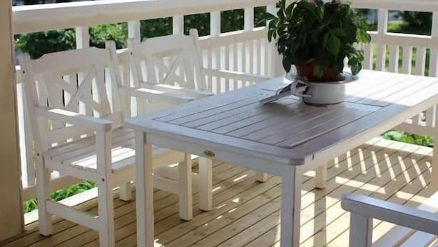 Una terraza de madera con muebles blancos, incluyendo una mesa y sillas, y una planta en maceta.