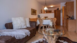 Un salon chaleureux avec un canapé marron, une table basse en verre et un coin repas comprenant une table et des chaises en bois.