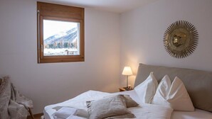 Une chambre à coucher avec un lit, une fenêtre donnant sur les montagnes, une lampe et un élément décoratif mural.