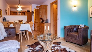 Un salon chaleureux avec une table basse en verre, un fauteuil en cuir et un coin repas doté de meubles en bois.