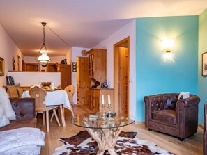 Ein gemütliches Wohnzimmer mit einem Glastisch, Ledersessel und einer Essecke mit Holzmöbeln.