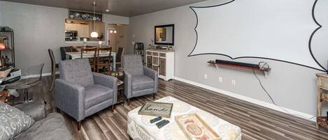 A living room with a sofa, two armchairs, a coffee table with a 'home' sign, and a patterned ottoman.