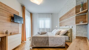 Quarto moderno com cama, paredes de madeira, televisão e janela com cortinas.