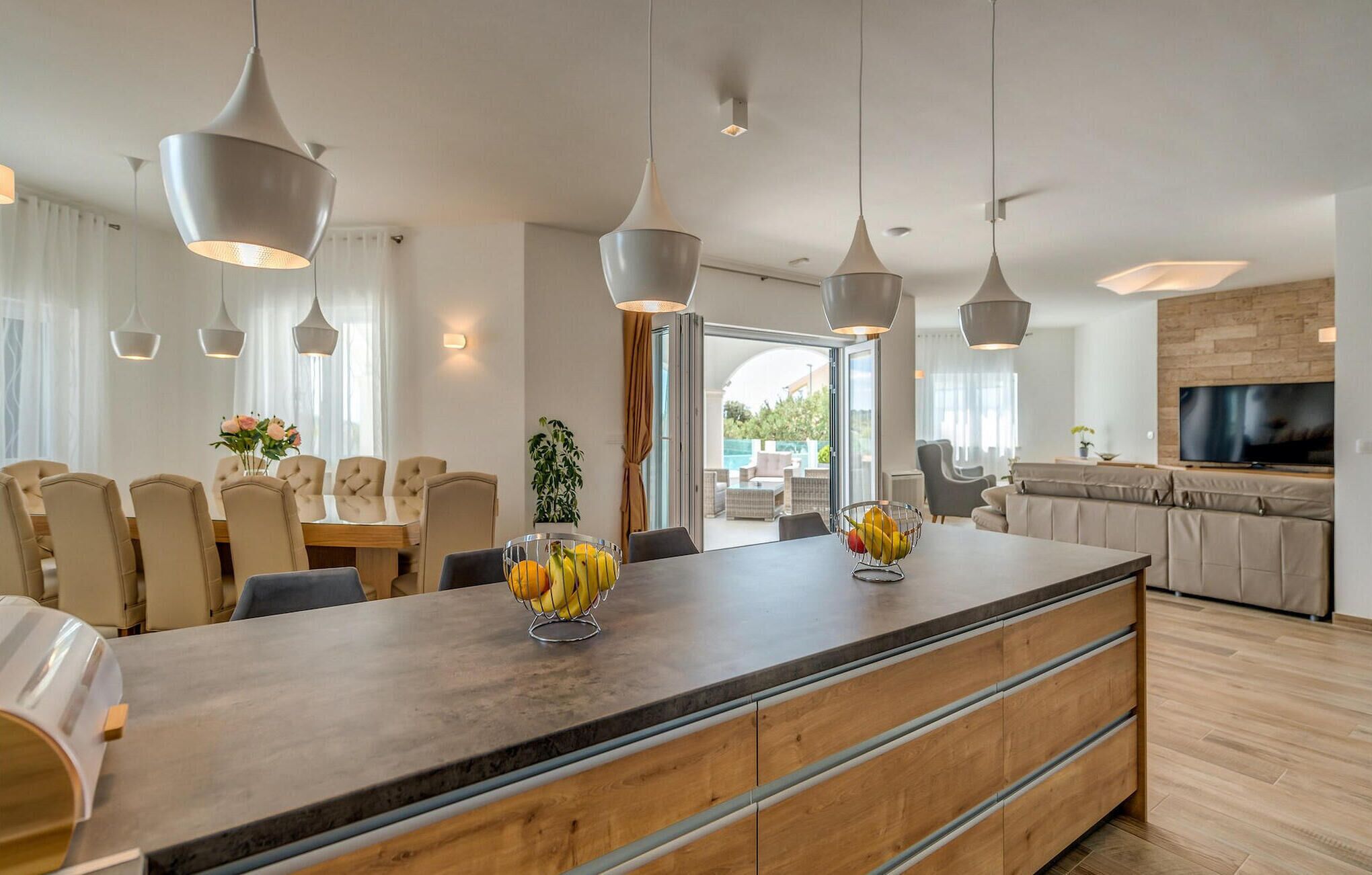 Een moderne keuken met een centraal eiland, hanglampen, en een zithoek met stoelen en een tafel.