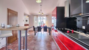 A modern kitchen with red cabinets, a stainless steel stove, and a dining area with a table and chairs.