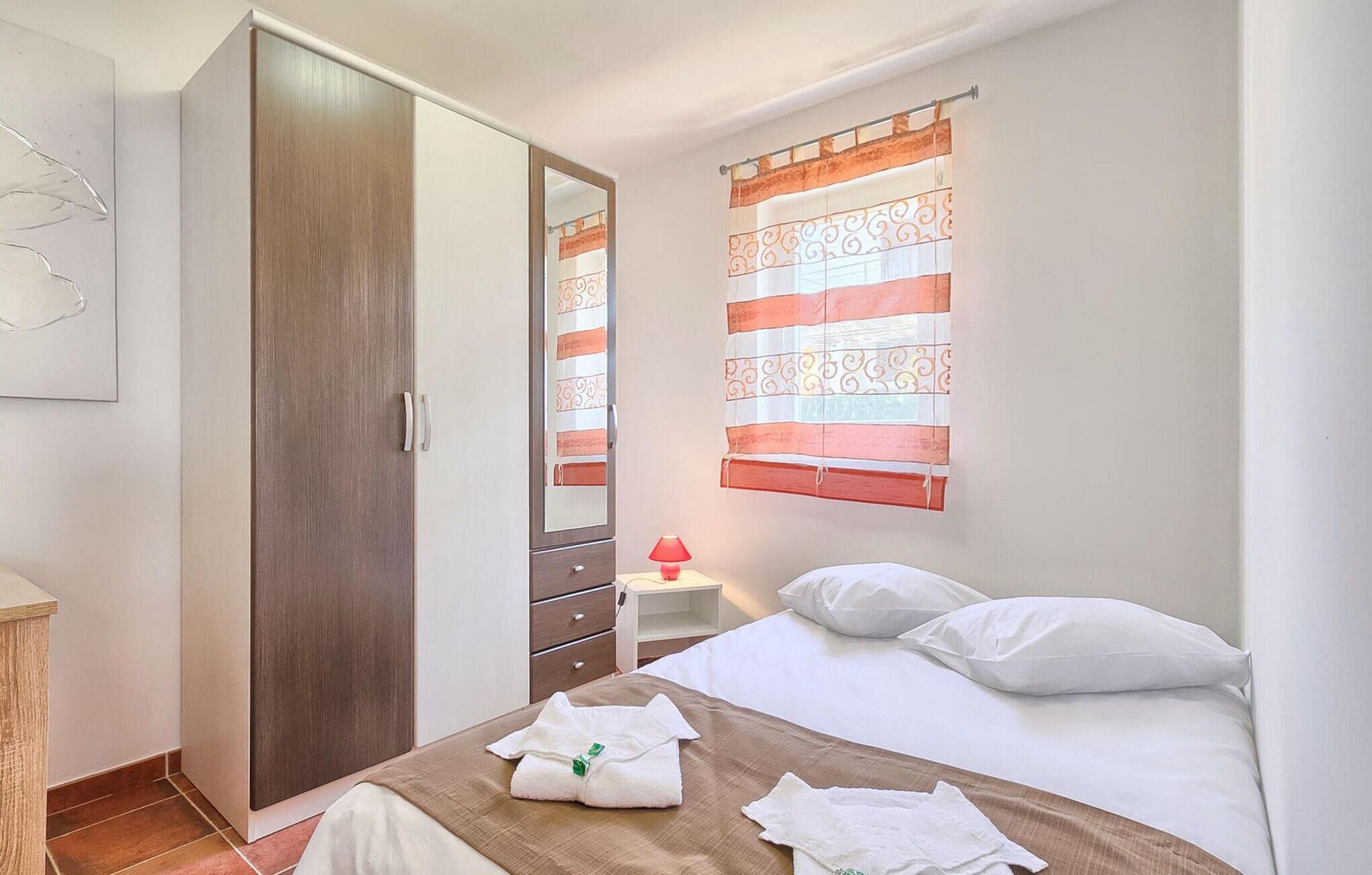 Une chambre à coucher comprenant un lit, une armoire, une table de chevet avec une lampe et une fenêtre avec des rideaux.