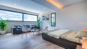 A modern bedroom with a large bed, a sofa, a coffee table, and two chairs. There is a window with a view of the sky and a plant on the left. - Beautiful home in Porec (Porec)