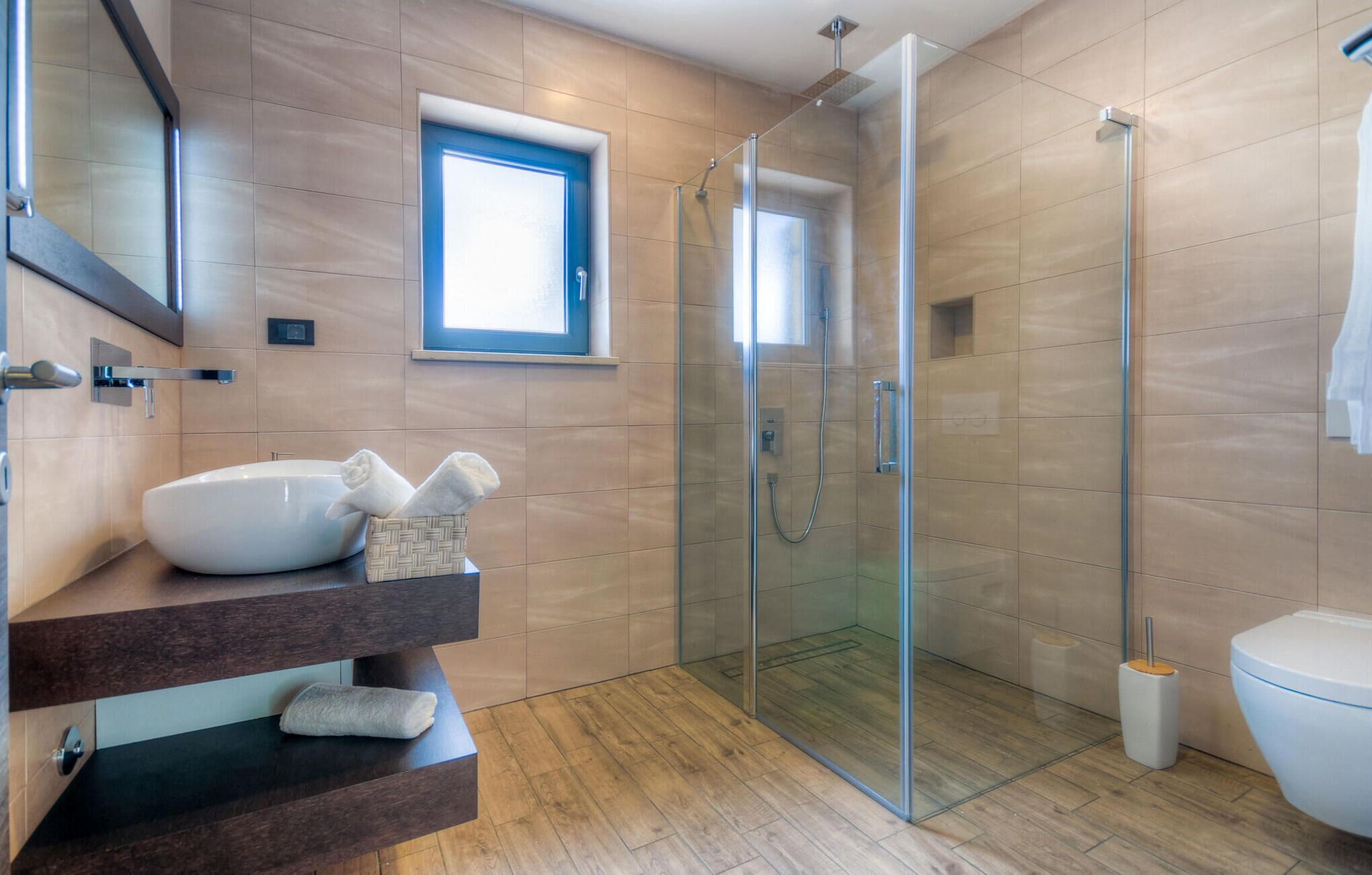 A modern bathroom with a glass-enclosed shower, a white sink, and a wooden vanity.