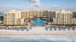 Un gran complejo turístico con varias edificaciones de hotel, una piscina central y una playa con tumbonas.