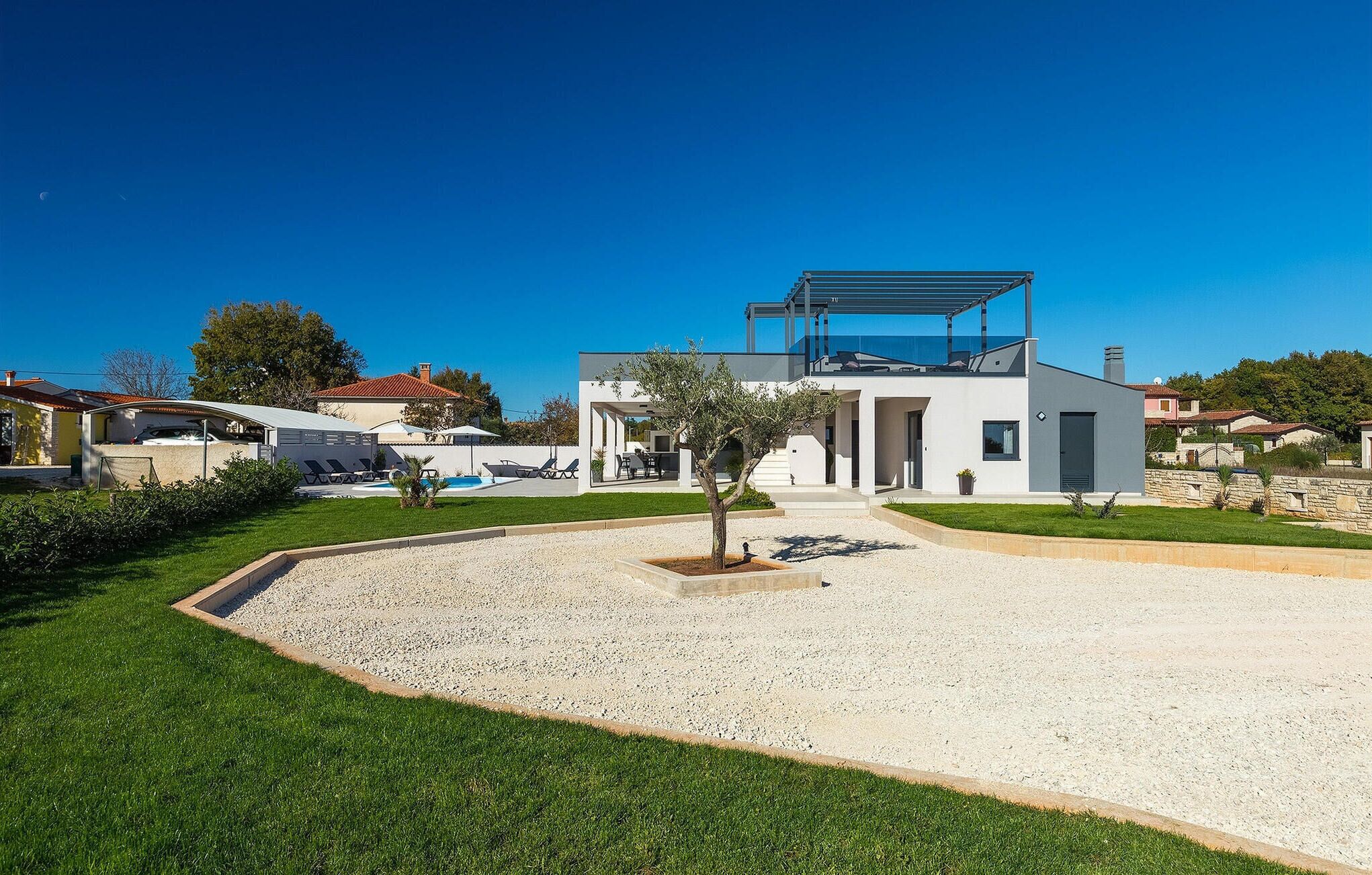 Et moderne hus med en overdækket terrasse, swimmingpool og en velplejet græsplæne.