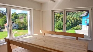 Una habitación con un banco de madera, ventanas amplias y vistas a un paisaje verde con casas.